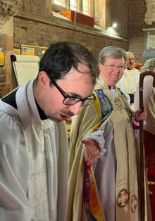 Slightly behind, Bishop Sarah gestures towards Dave as he bows his head during his priesting service